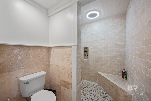 bathroom featuring toilet, a tile shower, and tile walls