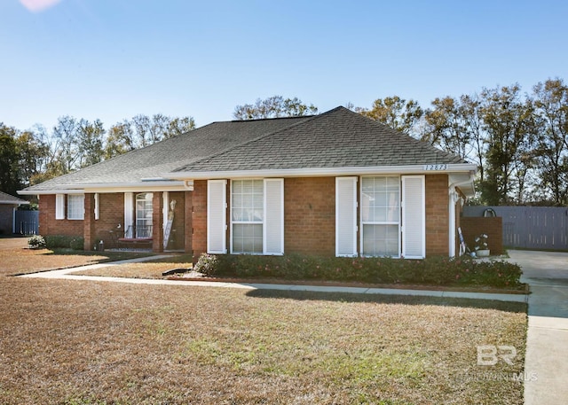 ranch-style home with a shingled roof, a front yard, brick siding, and fence