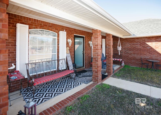 entrance to property featuring a shingled roof, a porch, and brick siding