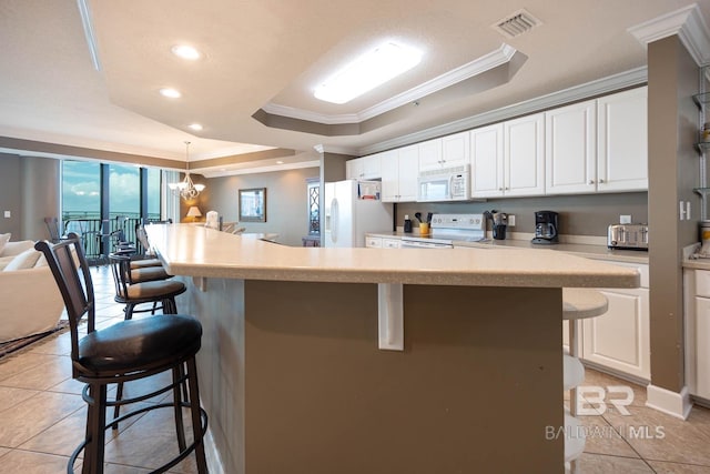 kitchen with an inviting chandelier, a raised ceiling, crown molding, white appliances, and a breakfast bar area