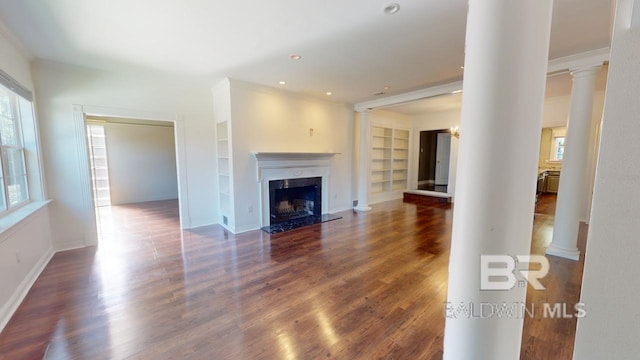 unfurnished living room with built in shelves, a premium fireplace, dark hardwood / wood-style floors, decorative columns, and crown molding