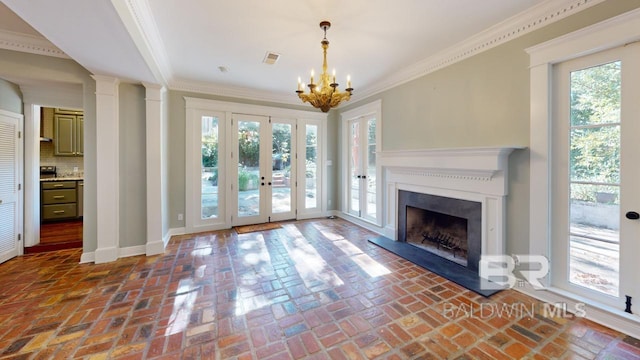 unfurnished living room with a wealth of natural light, crown molding, french doors, and an inviting chandelier