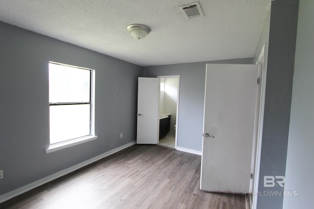 unfurnished bedroom featuring a textured ceiling, light hardwood / wood-style floors, and ensuite bath