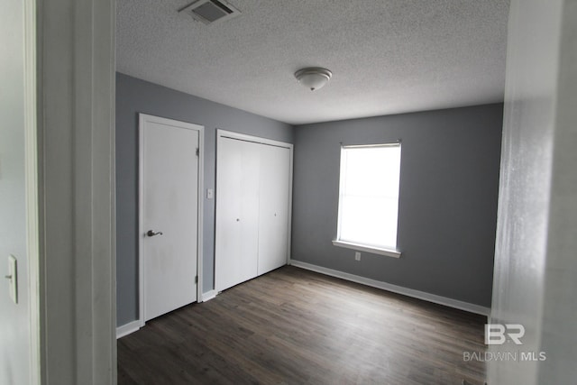 unfurnished bedroom featuring a textured ceiling, a closet, and dark hardwood / wood-style floors