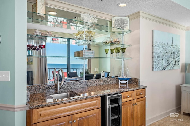 kitchen with sink, beverage cooler, dark stone countertops, a textured ceiling, and a water view