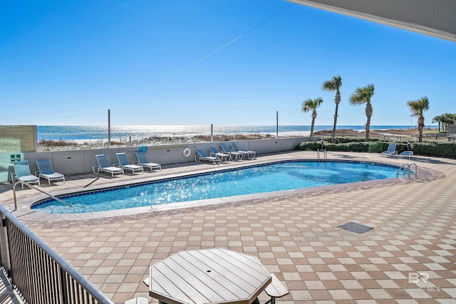 view of pool with a patio area, a water view, and a beach view