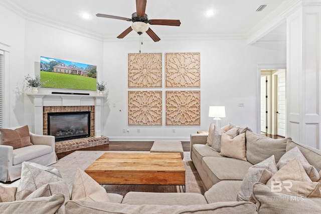 living room with a brick fireplace, ornamental molding, ceiling fan, wood-type flooring, and beam ceiling