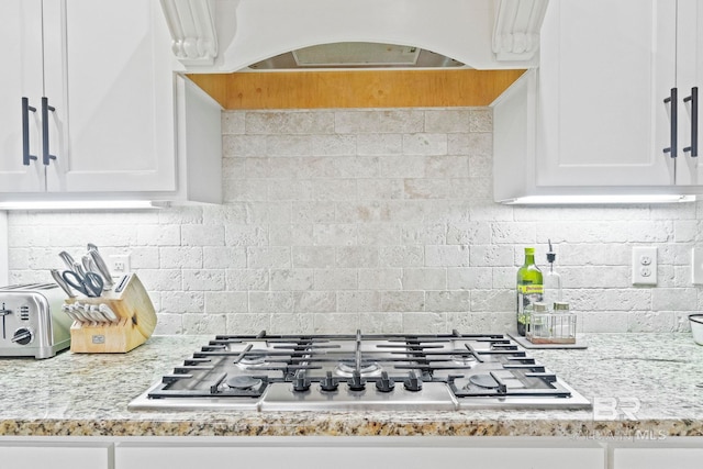 kitchen with decorative backsplash, white cabinets, light stone countertops, and stainless steel gas stovetop