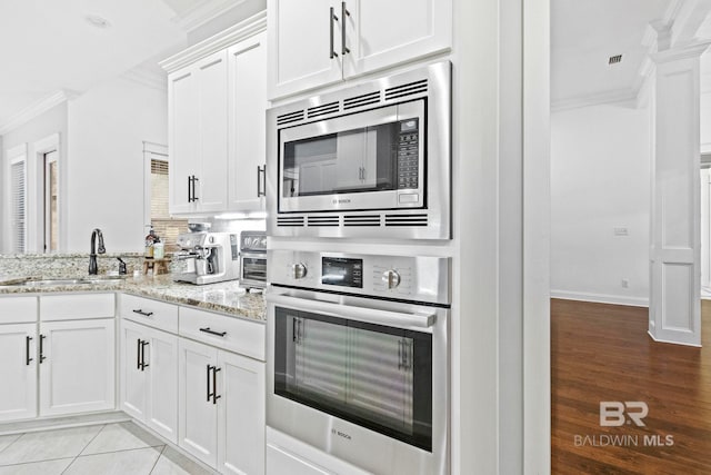 kitchen featuring white cabinets, appliances with stainless steel finishes, light stone countertops, and sink