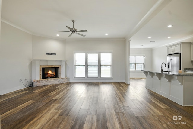 unfurnished living room featuring baseboards, a brick fireplace, dark wood-style flooring, and crown molding