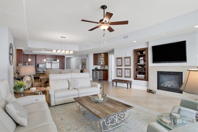 living area featuring light tile patterned floors, visible vents, a tiled fireplace, and ceiling fan with notable chandelier