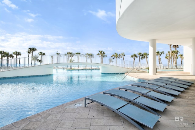 community pool with a patio, a water view, and fence