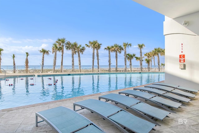 community pool with a water view, fence, and a patio