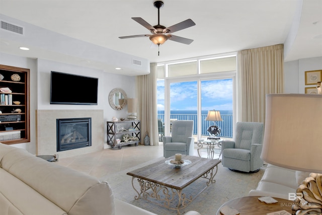 living room with built in features, visible vents, a tiled fireplace, expansive windows, and ceiling fan