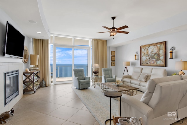 living room with a fireplace, a water view, expansive windows, light tile patterned flooring, and ceiling fan