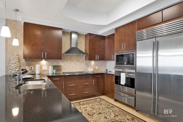 kitchen featuring decorative backsplash, built in appliances, a sink, wall chimney range hood, and a warming drawer