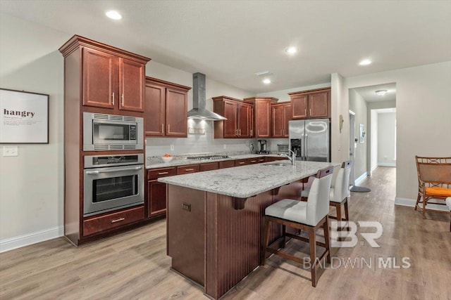 kitchen featuring appliances with stainless steel finishes, wall chimney range hood, baseboards, light wood finished floors, and recessed lighting