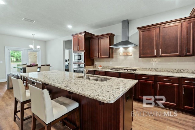 kitchen with wall chimney range hood, appliances with stainless steel finishes, light wood-style flooring, a sink, and recessed lighting