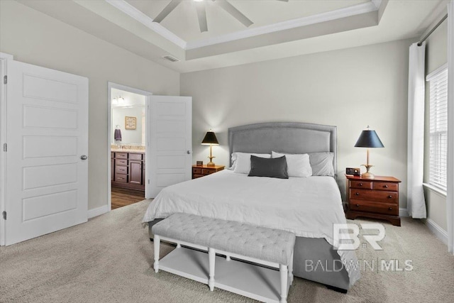 carpeted bedroom featuring a raised ceiling, ornamental molding, baseboards, connected bathroom, and ceiling fan