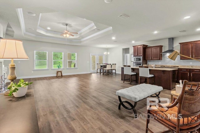 living area with a ceiling fan, wood finished floors, recessed lighting, ornamental molding, and baseboards