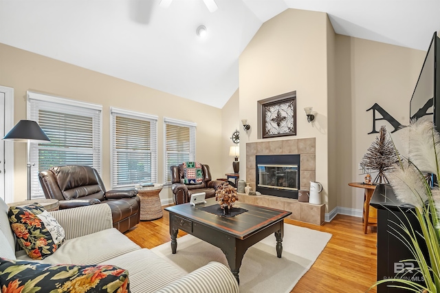 living room with ceiling fan, vaulted ceiling, a tile fireplace, and light hardwood / wood-style flooring