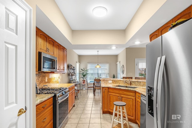 kitchen with sink, hanging light fixtures, light stone counters, light tile patterned flooring, and appliances with stainless steel finishes