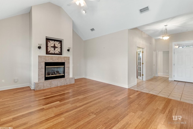 unfurnished living room with a tiled fireplace, ceiling fan, high vaulted ceiling, and light wood-type flooring