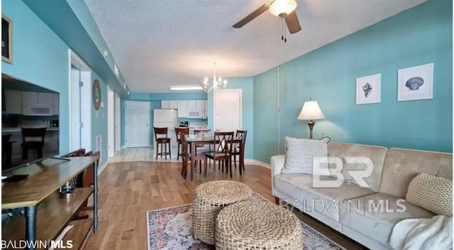 living room featuring ceiling fan with notable chandelier, light wood-type flooring, and a textured ceiling