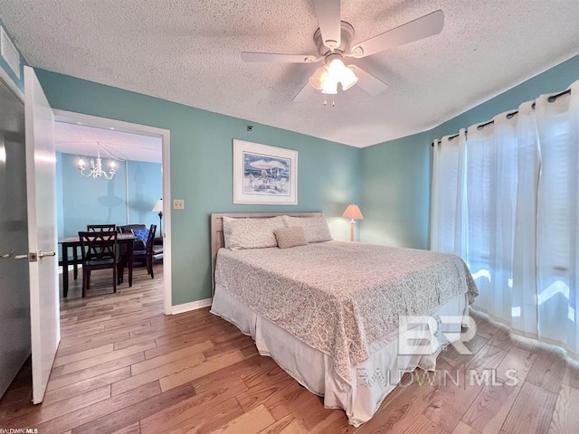 bedroom with ceiling fan with notable chandelier, a textured ceiling, and light hardwood / wood-style flooring