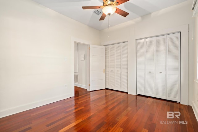 unfurnished bedroom with ceiling fan, dark hardwood / wood-style flooring, and two closets