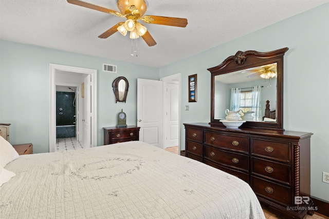 bedroom with visible vents, a textured ceiling, ensuite bathroom, and ceiling fan