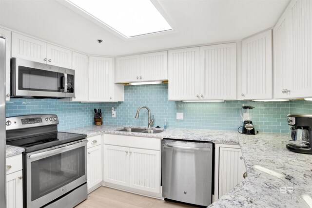 kitchen with white cabinets, sink, tasteful backsplash, light stone counters, and stainless steel appliances