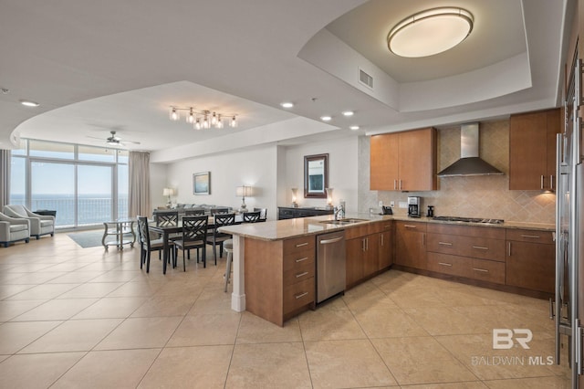 kitchen featuring stainless steel appliances, wall chimney range hood, a peninsula, and a raised ceiling