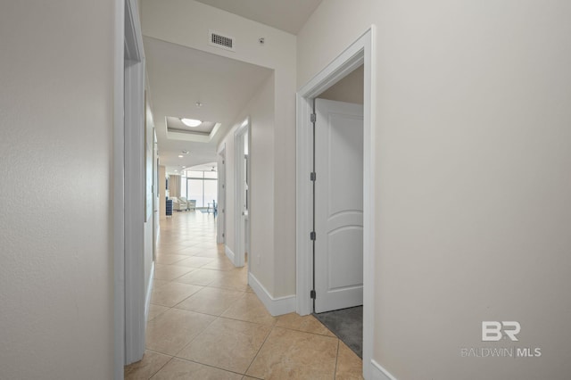 hallway with light tile patterned floors, baseboards, visible vents, and attic access