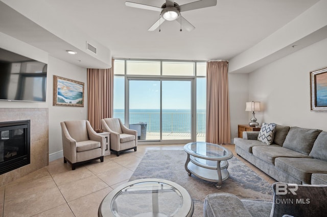 living room with light tile patterned flooring, a tile fireplace, a water view, visible vents, and floor to ceiling windows