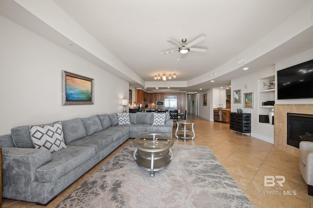 living area featuring built in shelves, a fireplace, light tile patterned floors, a ceiling fan, and baseboards