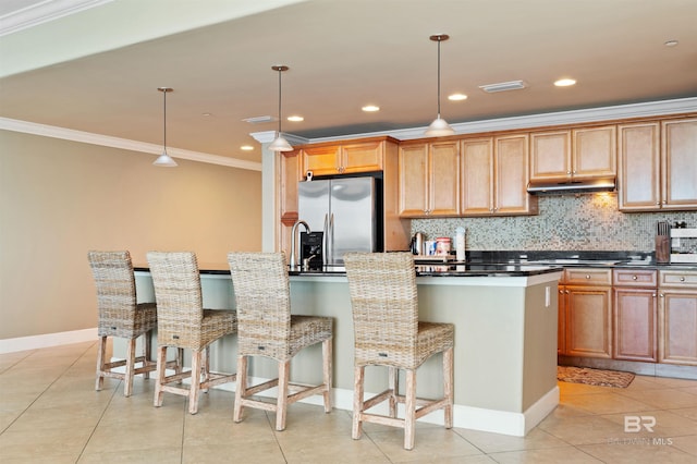 kitchen with ornamental molding, under cabinet range hood, tasteful backsplash, dark countertops, and stainless steel fridge with ice dispenser