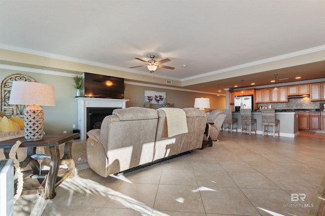 living room with light tile patterned floors, ceiling fan, a fireplace, and crown molding