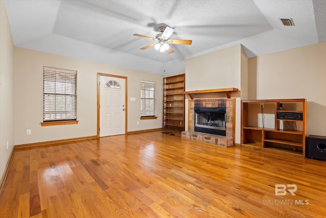 unfurnished living room featuring hardwood / wood-style floors, ceiling fan, a fireplace, a textured ceiling, and a tray ceiling