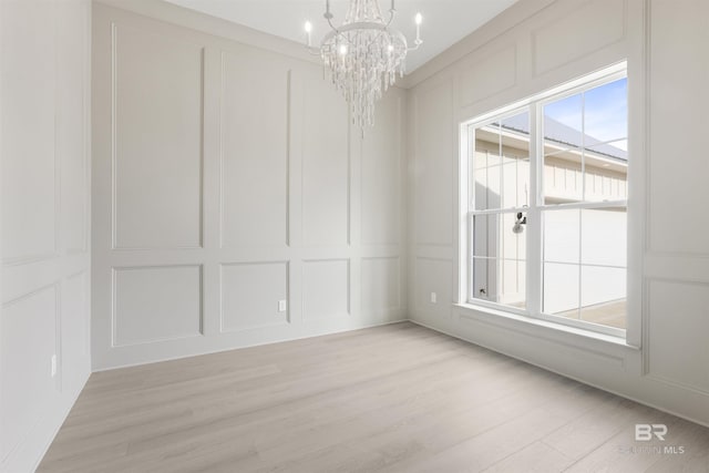 empty room with a notable chandelier, light wood-style floors, and a decorative wall