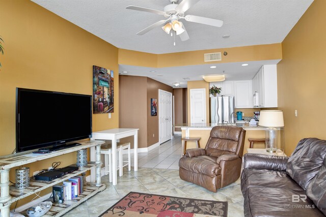 living area featuring visible vents, a ceiling fan, light tile patterned flooring, baseboards, and a textured ceiling