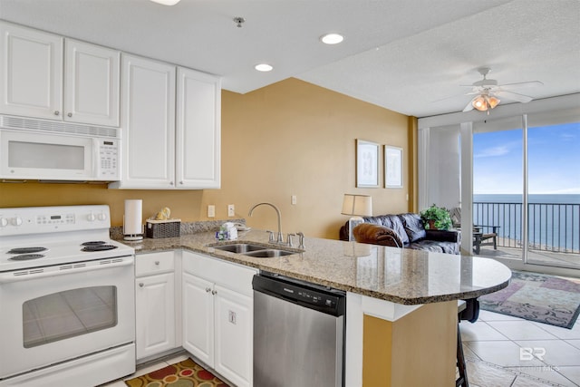 kitchen featuring a sink, white appliances, a wall of windows, white cabinets, and a peninsula