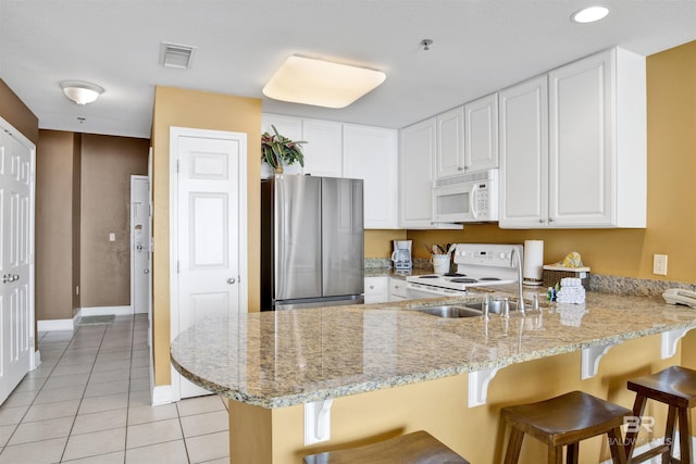 kitchen with visible vents, white appliances, light tile patterned flooring, a peninsula, and white cabinetry