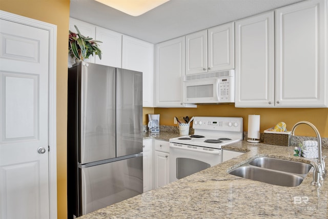 kitchen with white cabinetry, light stone countertops, a sink, and white appliances