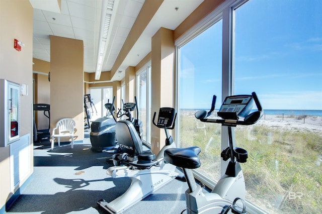 workout area with a beach view, a paneled ceiling, and a water view
