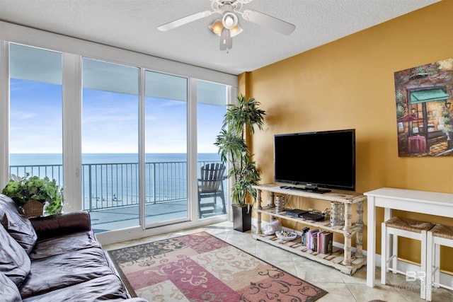 living room with a textured ceiling, a water view, tile patterned floors, and ceiling fan