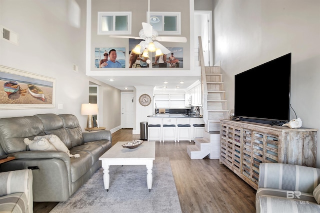 living area with wood finished floors, baseboards, visible vents, a high ceiling, and ceiling fan