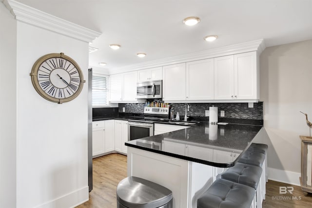 kitchen with a peninsula, a kitchen breakfast bar, white cabinets, and stainless steel appliances