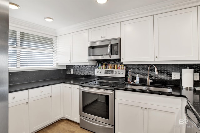 kitchen with a sink, backsplash, white cabinetry, appliances with stainless steel finishes, and light wood finished floors