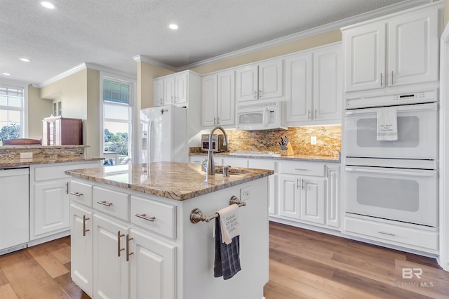 kitchen with light hardwood / wood-style flooring, a kitchen island with sink, sink, and white appliances